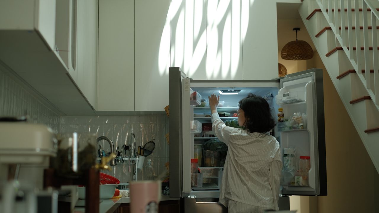 portfolio-04 A woman in pajamas checks the refrigerator in a warmly lit cozy kitchen.
